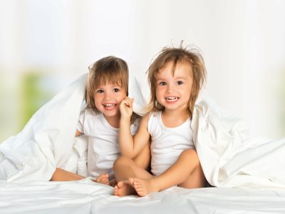 happy little girl’s twin sister in bed under the blanket having fun, smiling happy little girl's twin sister in bed under the blanket having fun, smiling